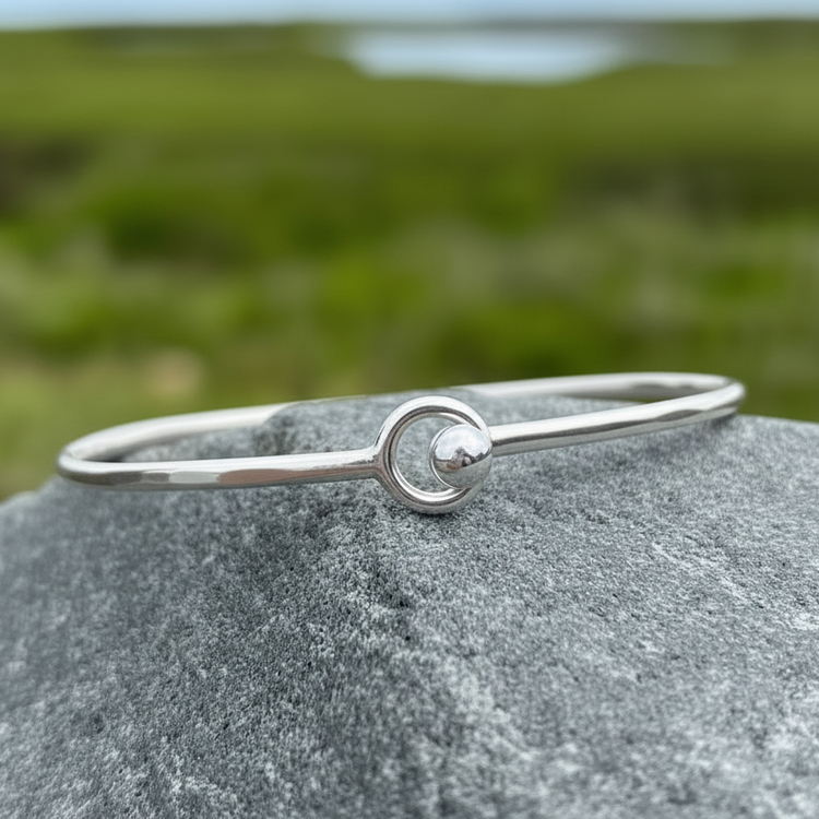Sterling silver bangle bracelet with silver ball accent on a coastal rock