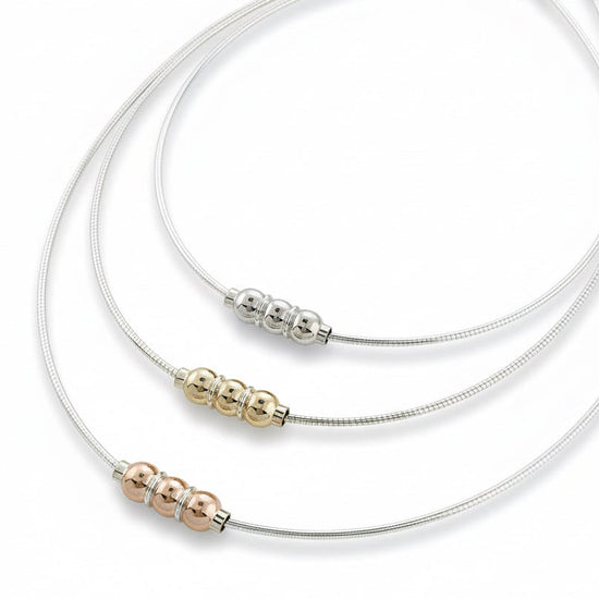 A collection of Cape Cod triple ball omega necklaces in silver with varying lengths, displayed on a flat surface.