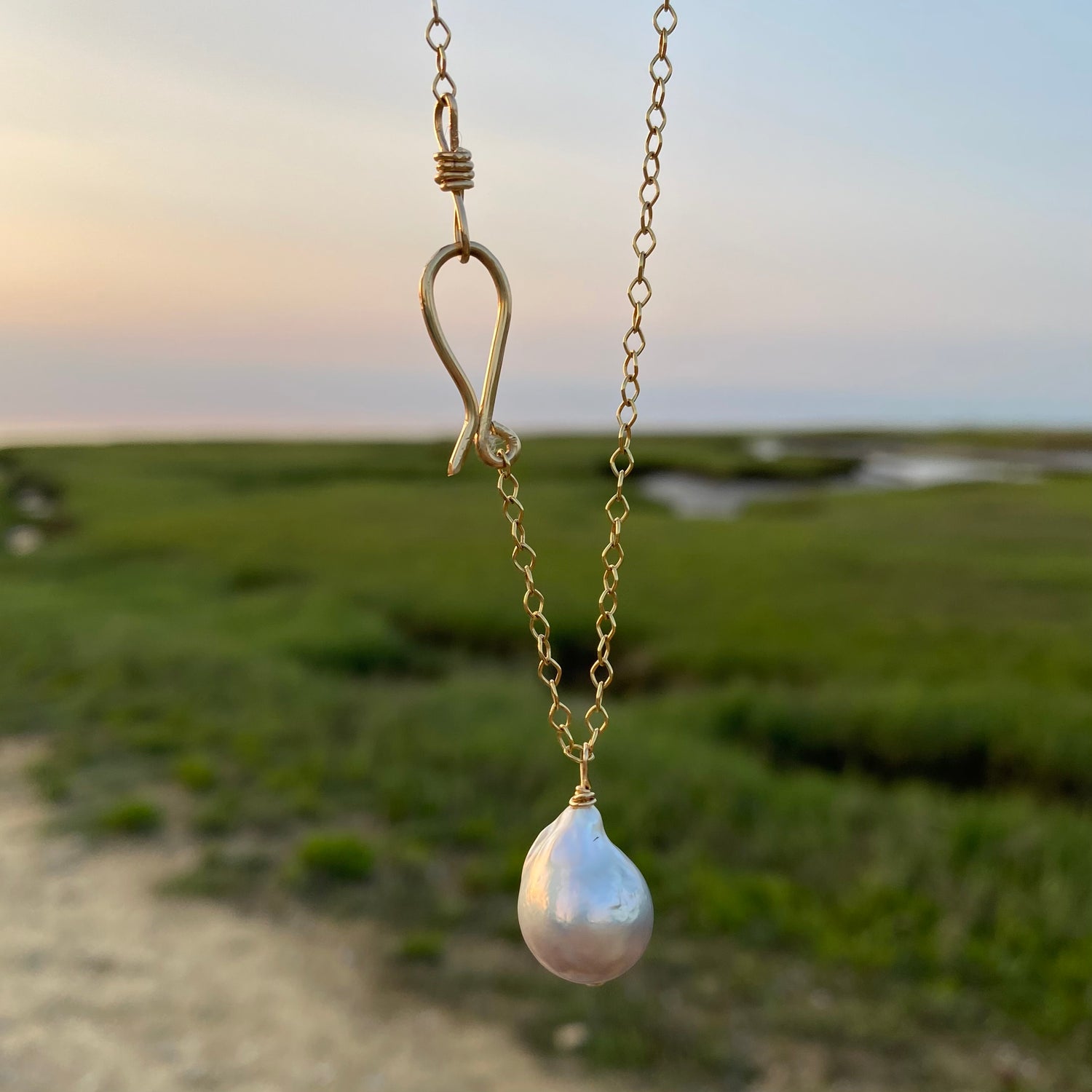 A baroque pearl long sea drop necklace with a gold-filled chain, displayed against an outdoor backdrop.