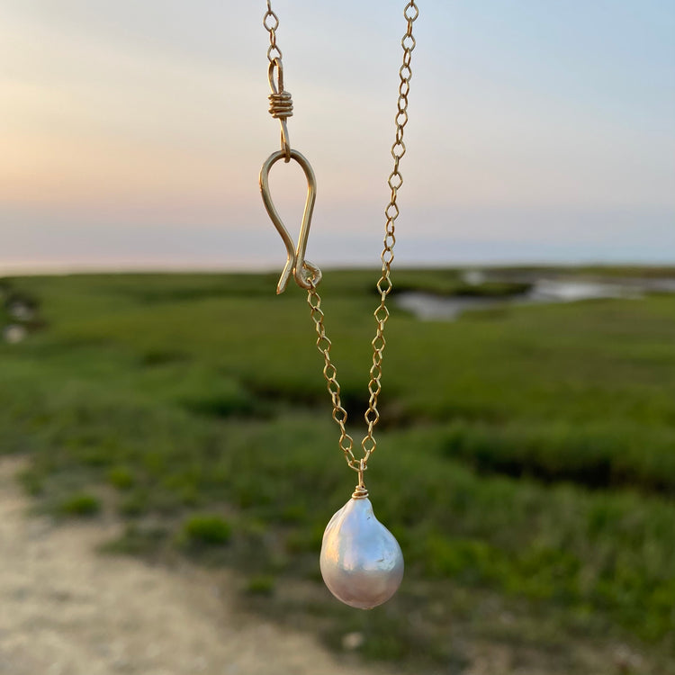 A baroque pearl long sea drop necklace with a gold-filled chain, displayed against an outdoor backdrop.