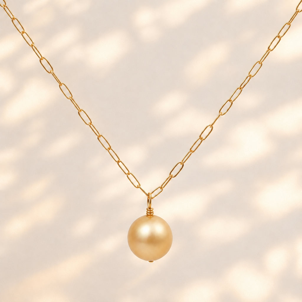 A gold chain necklace featuring a single round, lustrous gold pearl pendant, displayed against a clean white background.
