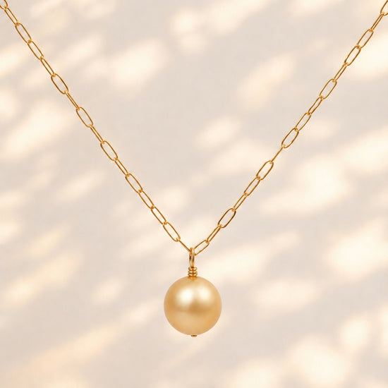 A gold chain necklace featuring a single round, lustrous gold pearl pendant, displayed against a clean white background.