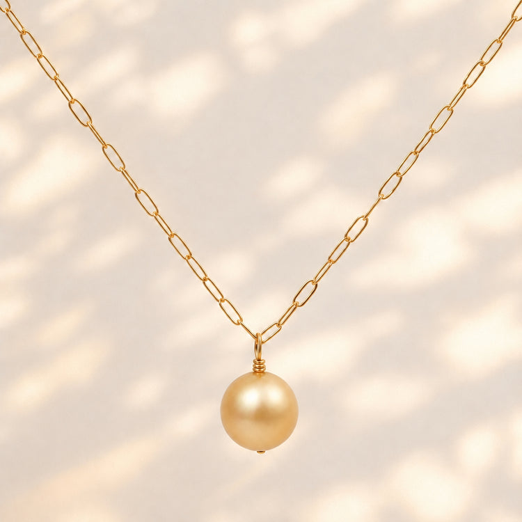 A gold chain necklace featuring a single round, lustrous gold pearl pendant, displayed against a clean white background.