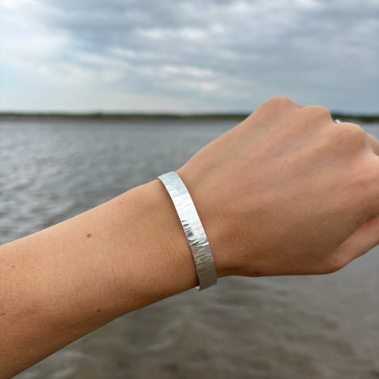 Silver bracelet on a wrist with a blurred water background