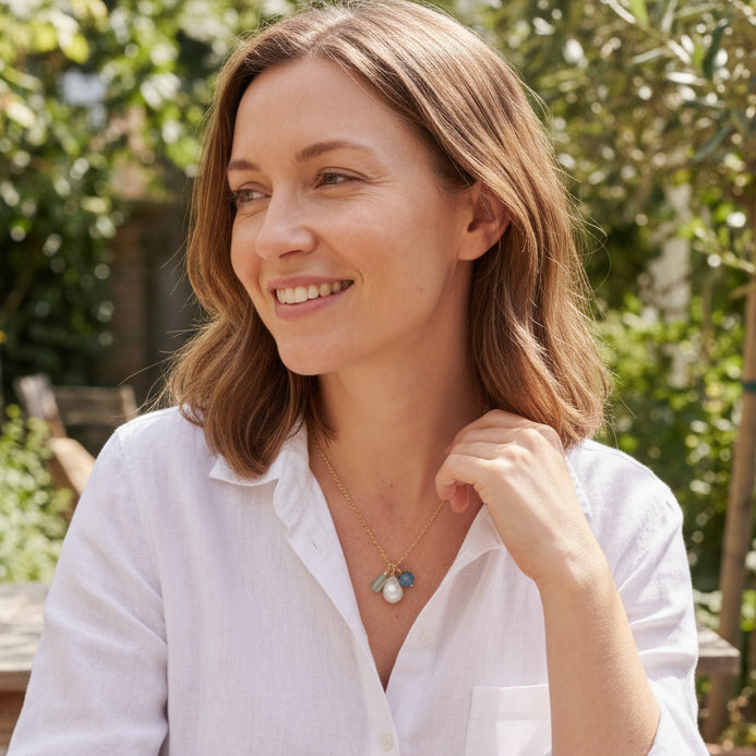 Woman in a white-colored shirt sitting outdoors with greenery in the background