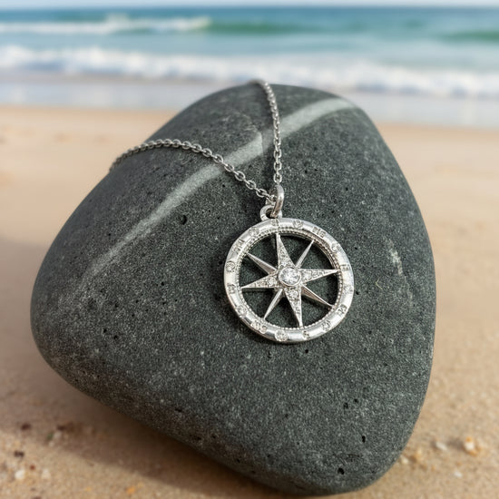 White gold and diamond compass pendant necklace on a dark stone surface