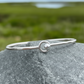 Sterling silver bangle bracelet with silver ball accent on a coastal rock