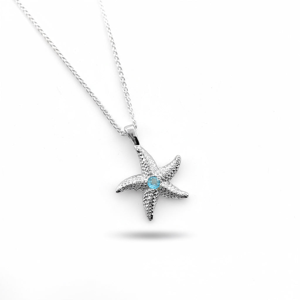 A sterling silver starfish pendant necklace with a blue topaz gemstone in the center, displayed on a white background.
